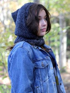 a young woman wearing a denim jacket and a knitted hoodie looks off into the distance