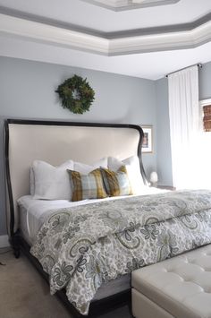 a bedroom with a bed, ottoman and wreath hanging on the wall above it's headboard