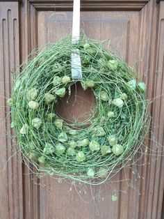 a wreath is hanging on the front door with green flowers and leaves around it,