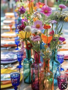 the table is set with colorful glass vases and place settings for guests to sit at