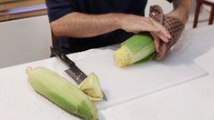 a man cutting up some corn on top of a white board with a large knife