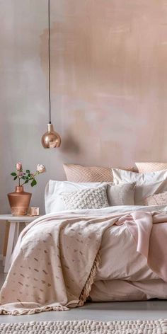 a bed with pink linens and pillows in a white room next to a wall