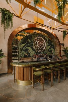 the bar is decorated with green plants and gold barstools in front of an arched glass window