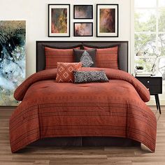 a bed with orange comforter and pillows in a room next to pictures on the wall