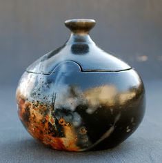 a small black vase sitting on top of a table next to a gray cloth covered floor