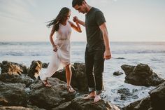 a man and woman standing on rocks near the ocean