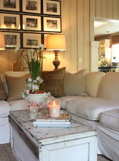 a living room filled with white furniture and pictures on the wall above it's coffee table