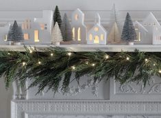 a fireplace mantel decorated with christmas trees and lit up houses on top of it