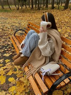 a woman is sitting on a park bench with her headphones in her ears and holding a coffee cup