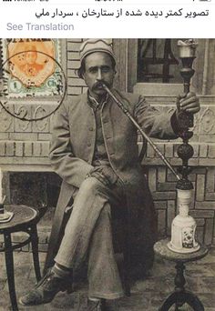 an old black and white photo of a man sitting on a chair holding a pipe