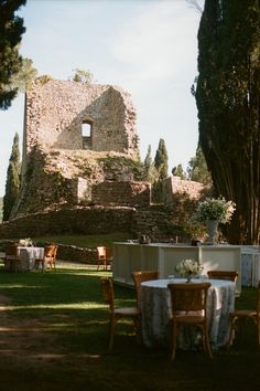 an outdoor dining area with tables and chairs in front of a stone building surrounded by trees