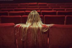 the back of a woman's head as she sits in an empty theater seat