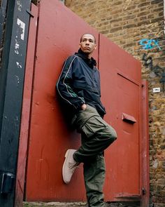 a man leaning against a red door in front of a brick building