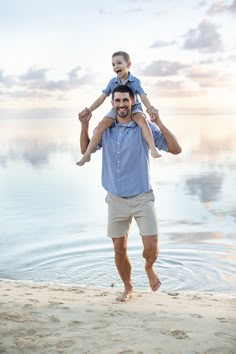 a man holding a little boy on his shoulders while standing in front of the ocean