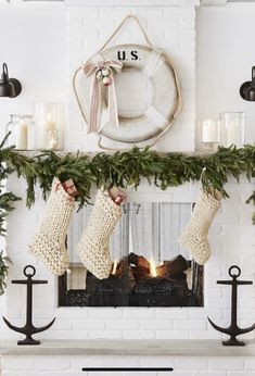 christmas stockings hanging from the mantel in front of a fireplace with candles and wreaths