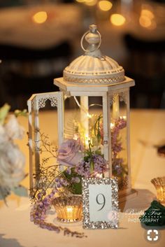 a table topped with a white lantern filled with flowers