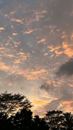 the sky is filled with clouds as the sun sets in the distance behind some trees