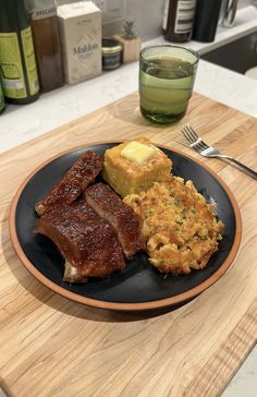 a plate with ribs, hash browns and bread on it next to a glass of wine