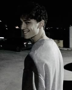 a black and white photo of a young man smiling at the camera with his hands in his pockets