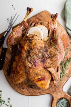 a whole turkey on a wooden cutting board with knifes and herbs next to it