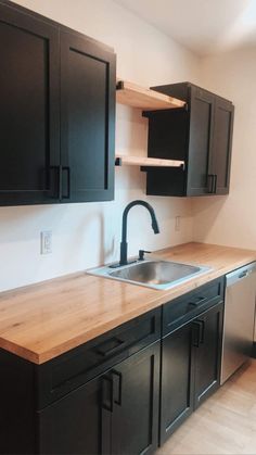 an empty kitchen with black cabinets and wooden counter tops, including a stainless steel sink