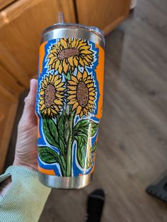 a person holding up a can with sunflowers painted on it