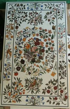 an intricately designed tile with flowers and leaves on it's border, in the process of being painted