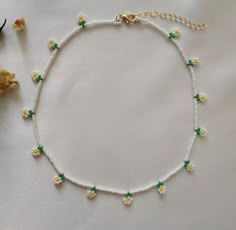 a white beaded necklace with yellow and green beads on it next to a flower