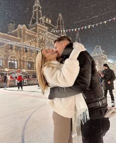 a man and woman kissing in front of a building on an ice rink at night