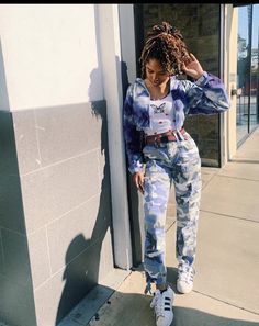 a woman standing on the sidewalk with her hand in her hair and wearing blue jeans