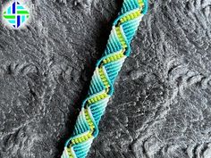 a blue and yellow braided bracelet on top of a gray surface with a logo in the background