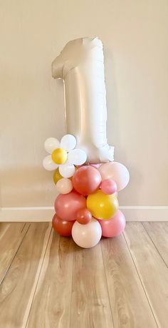 a bunch of balloons sitting on top of a wooden floor next to a giant number one balloon