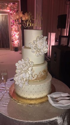 a three tiered wedding cake with white flowers and gold trim on a silver table