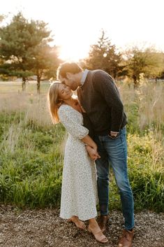 an engaged couple kissing in the field at sunset