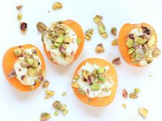 three oranges with nuts and cream on them are sitting on a white surface next to some pistachio seeds