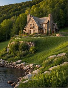 a stone house sitting on top of a lush green hillside next to a body of water