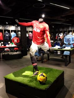 a display case filled with mannequins and soccer balls on fake grass in a store