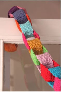 a multicolored crocheted bracelet hanging from a window sill in front of a mirror