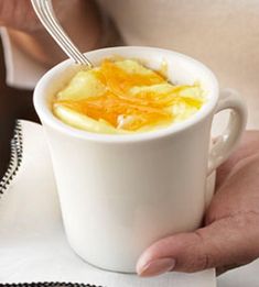 a person holding a white cup filled with orange juice and topped with a spoon in it