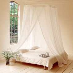 a white canopy bed sitting on top of a hard wood floor next to a window