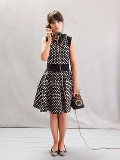 a woman in a polka dot dress is talking on the phone and holding a purse