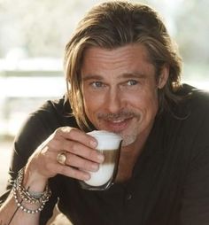 a man with long hair holding a glass of milk in his hand and smiling at the camera