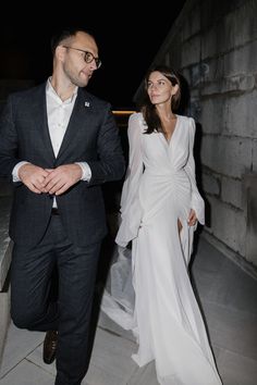 a man in a suit and tie walking next to a woman wearing a white dress