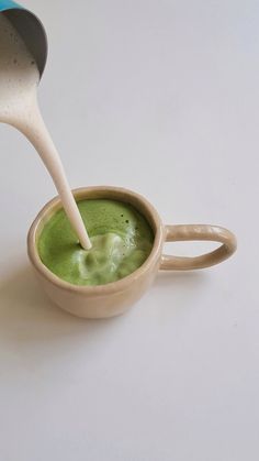 a cup filled with green liquid being poured into the cup by a spoon on a white surface