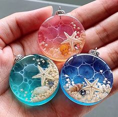 three small glass pendants with shells and starfish on them in the palm of someone's hand