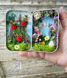 a hand holding an open tin box with flowers inside