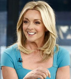 a woman with blonde hair and blue shirt sitting in front of a tv screen smiling at the camera