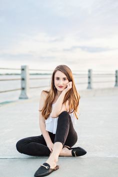 a young woman sitting on the ground with her legs crossed and wearing black pants, white tank