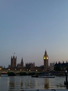 the big ben clock tower towering over the city of london at dusk with boats in the river below