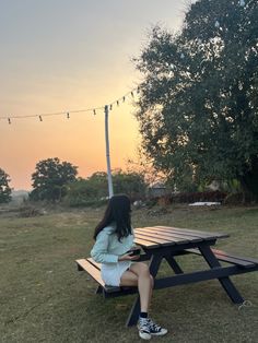 a woman sitting at a picnic table with string lights strung above her and trees in the background